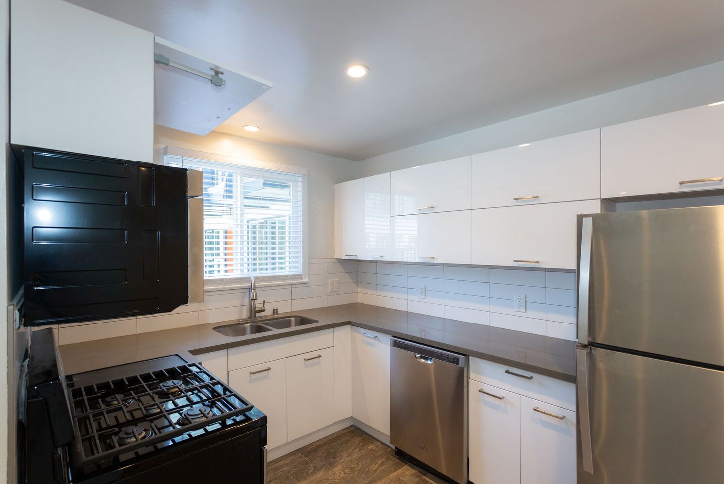 Modern white kitchen with stainless steel appliances, gas stove, dishwasher, and window above the sink
