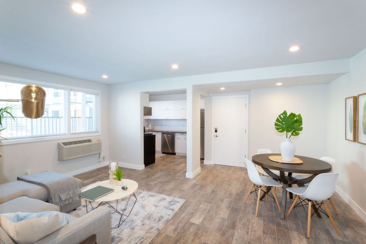 Bright open living-dining room with gray sofa, round table, wood floors, and white walls
