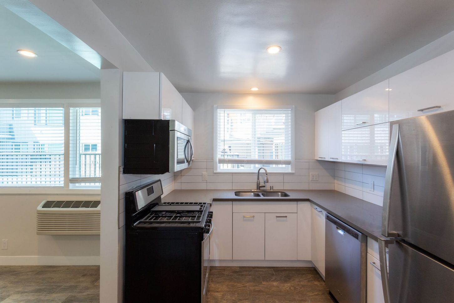 Bright kitchen with white cabinets, black stove, stainless fridge, and large windows.