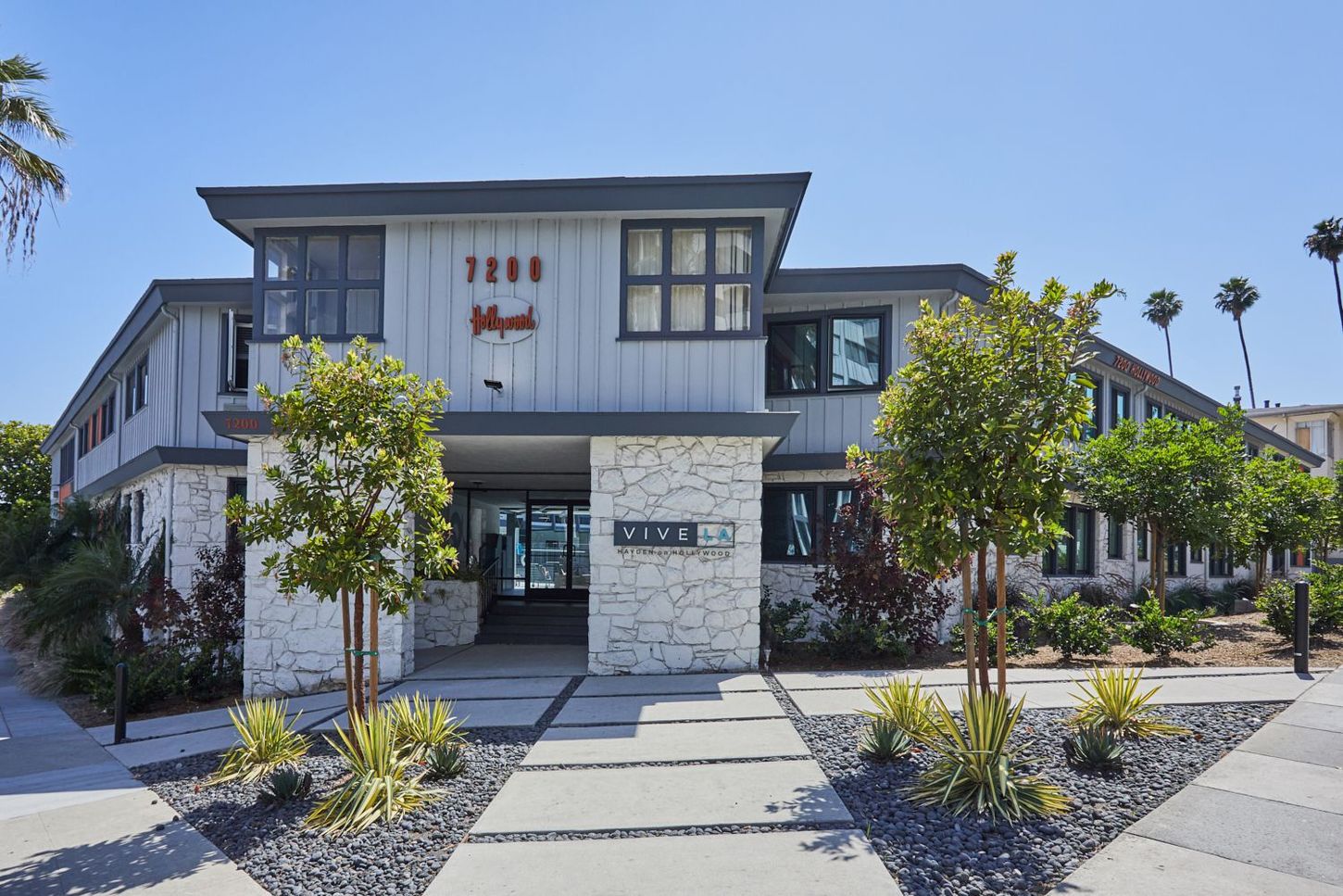 Modern two-story apartment building with landscaped walkway and trees in front