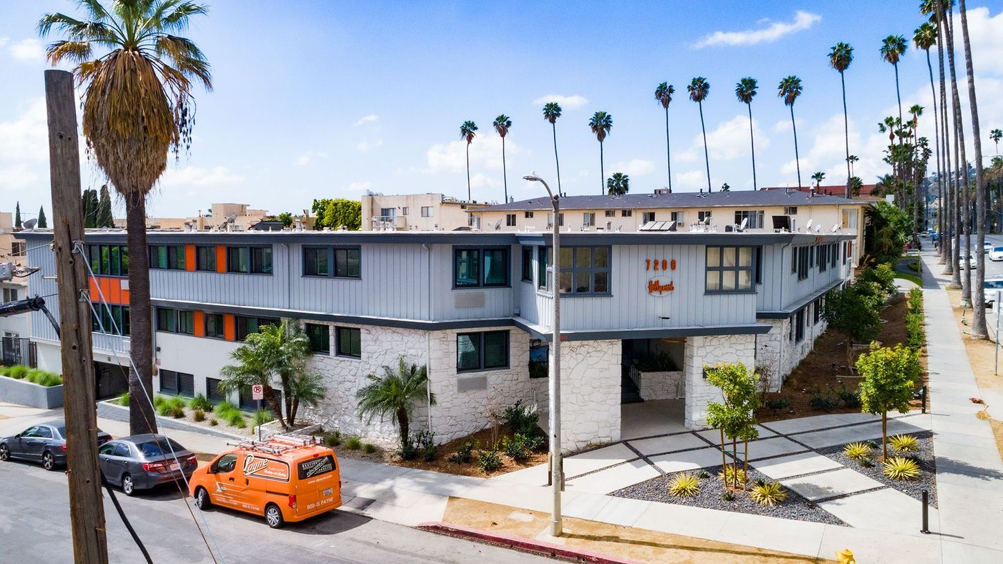 Modern apartment building on a sunny street with palm trees and parked orange van