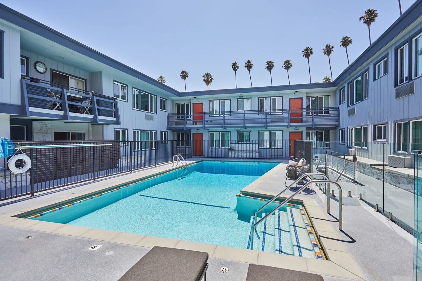 Apartment courtyard with a turquoise pool, white railings, and two-story buildings under palm trees