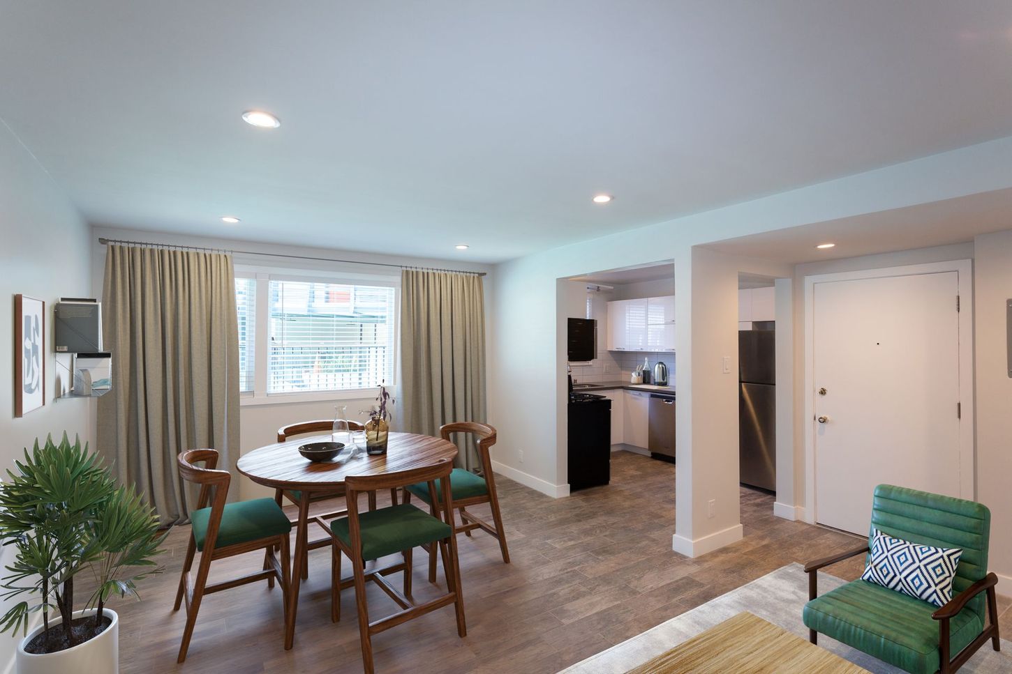 Bright dining room with a round table, chairs, large window, and open view into a kitchen.