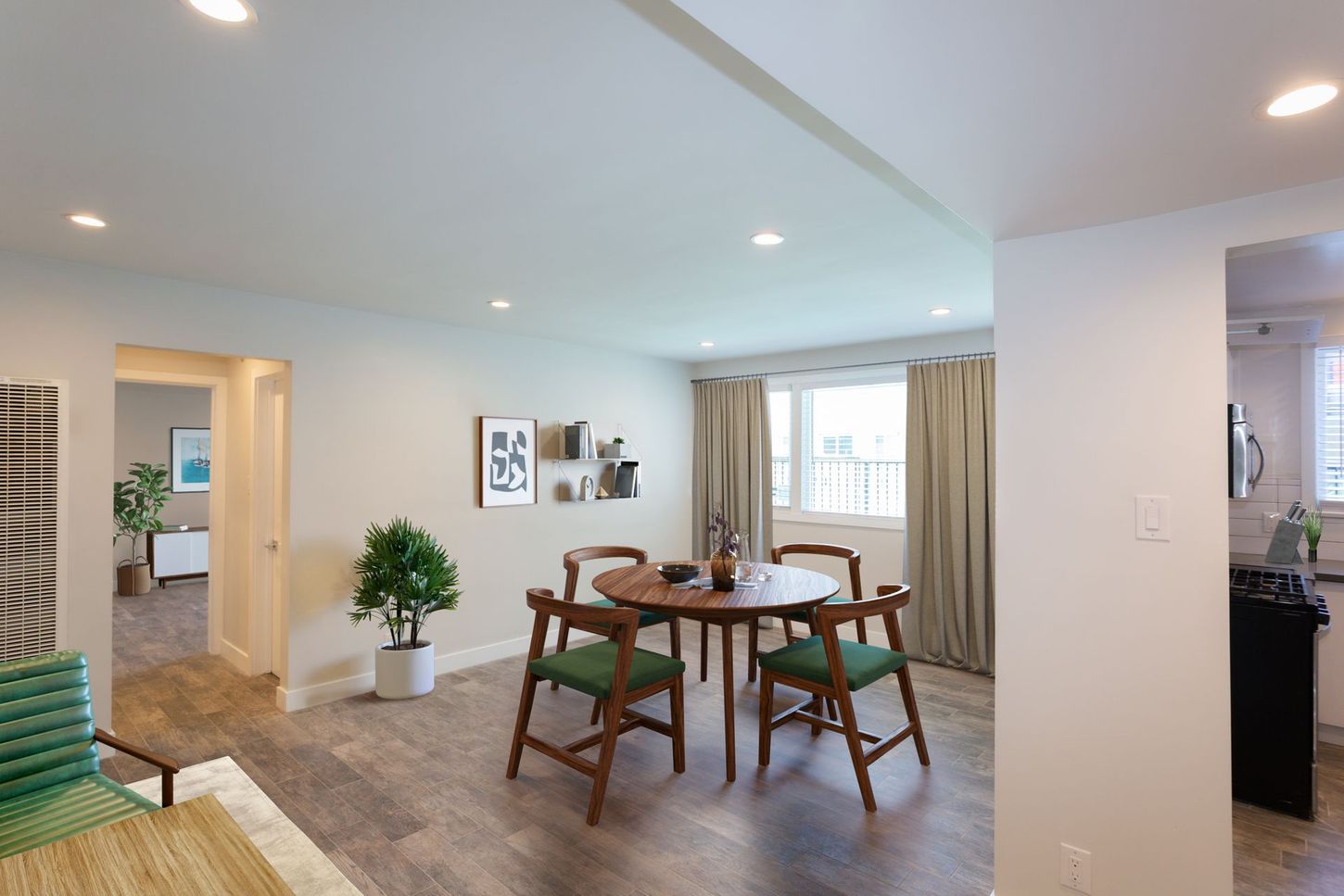 Bright open dining room with a wooden table, chairs, potted plant, and large windows with curtains.