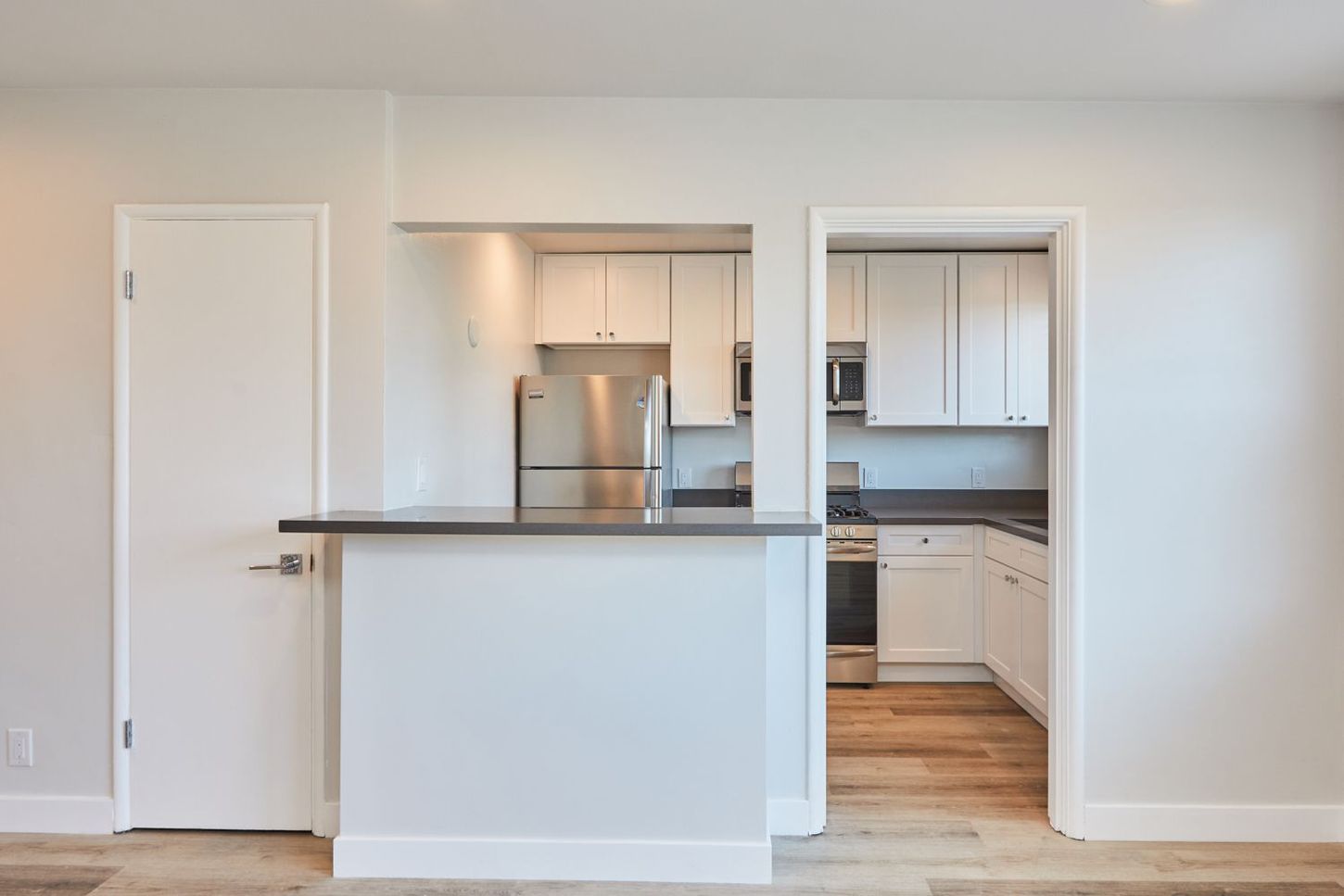 Bright open kitchen with white cabinets, stainless appliances, and a pass-through counter in a modern apartment.