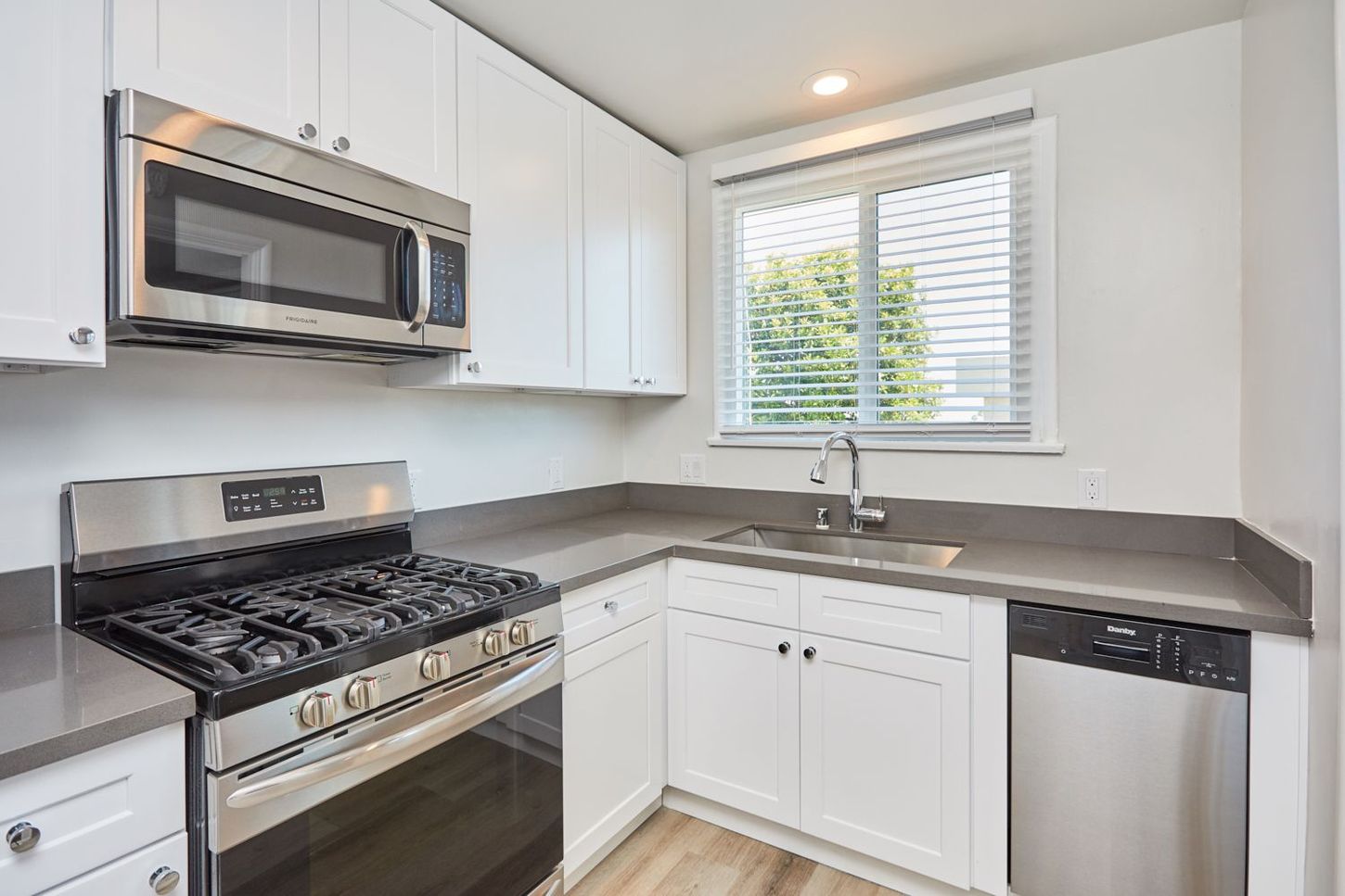 Modern white kitchen with stainless steel appliances, gray countertops, and a window over the sink