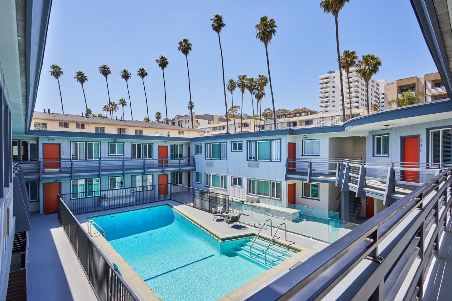 Courtyard apartment complex with a blue swimming pool and palm trees under a clear sky
