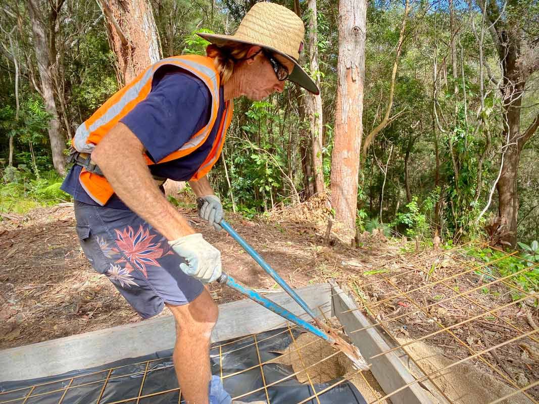 A Man Wearing a Straw Hat and Safety Vest Is Working on A Fence — Shaka Concreting In South Golden Beach, NSW