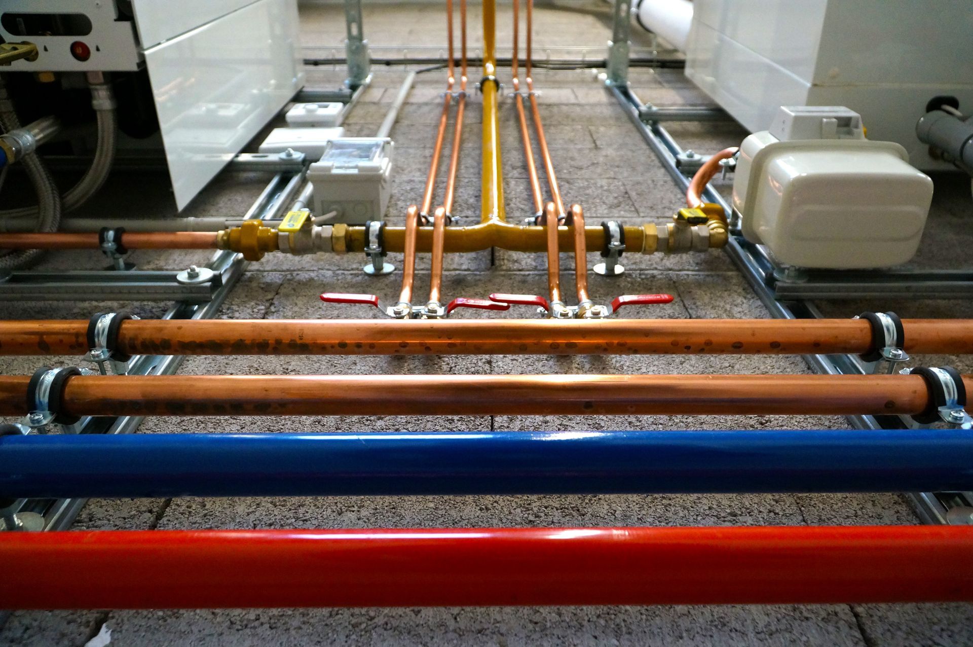 Industrial pipes and cables running along a floor, with orange and red tubing in a workshop setting