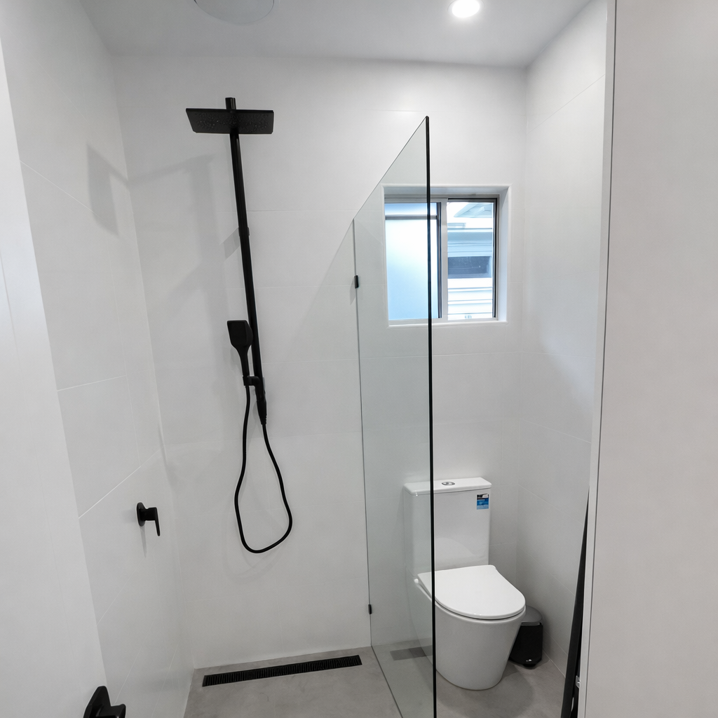 Modern white bathroom with black shower fixtures, glass partition, and toilet.