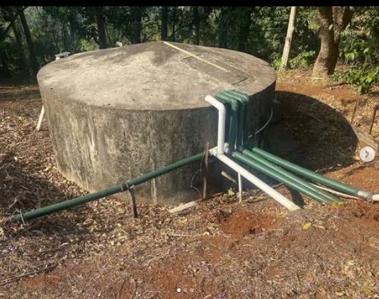 Large, round concrete water tank outdoors with connected green and white pipes.