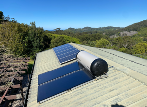 Solar panels and water heater on a rooftop overlooking a green landscape under a blue sky.