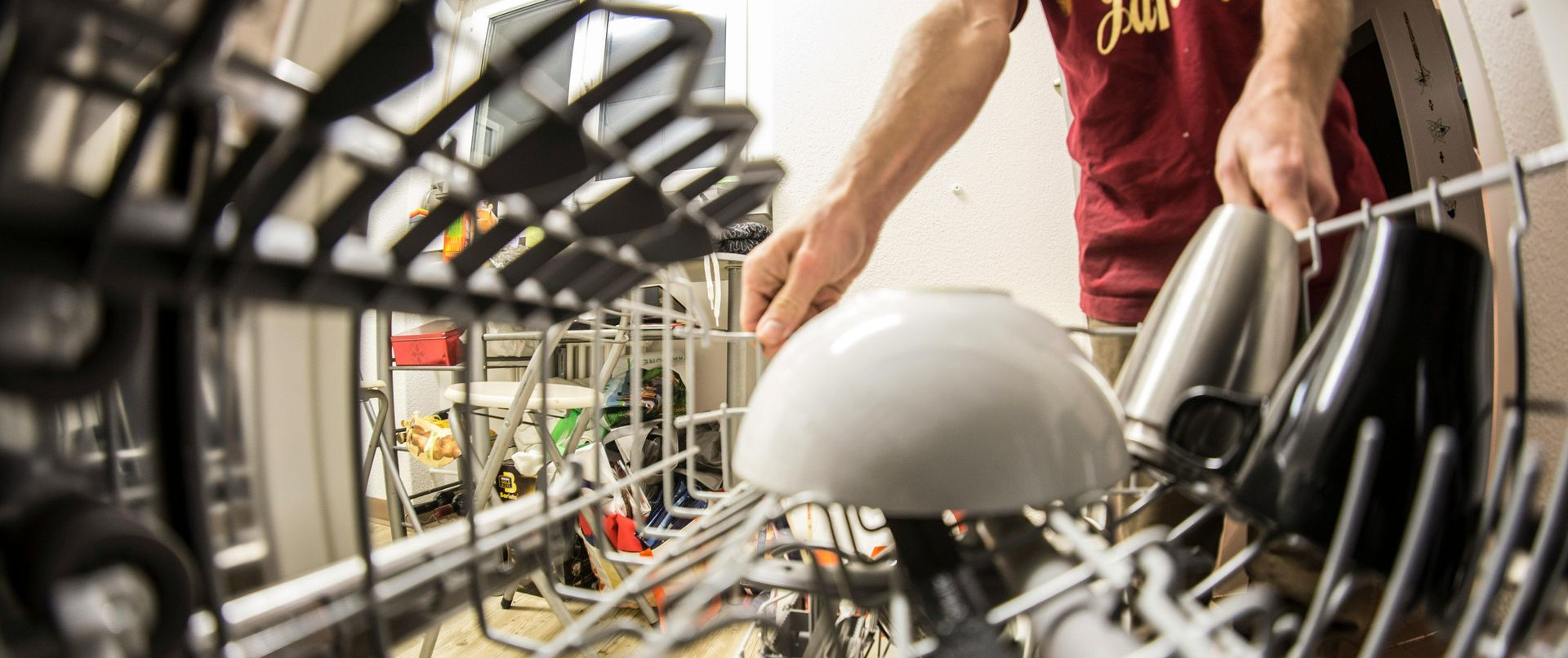 Person loading a white bowl into a dishwasher. Other dishes are already loaded inside.