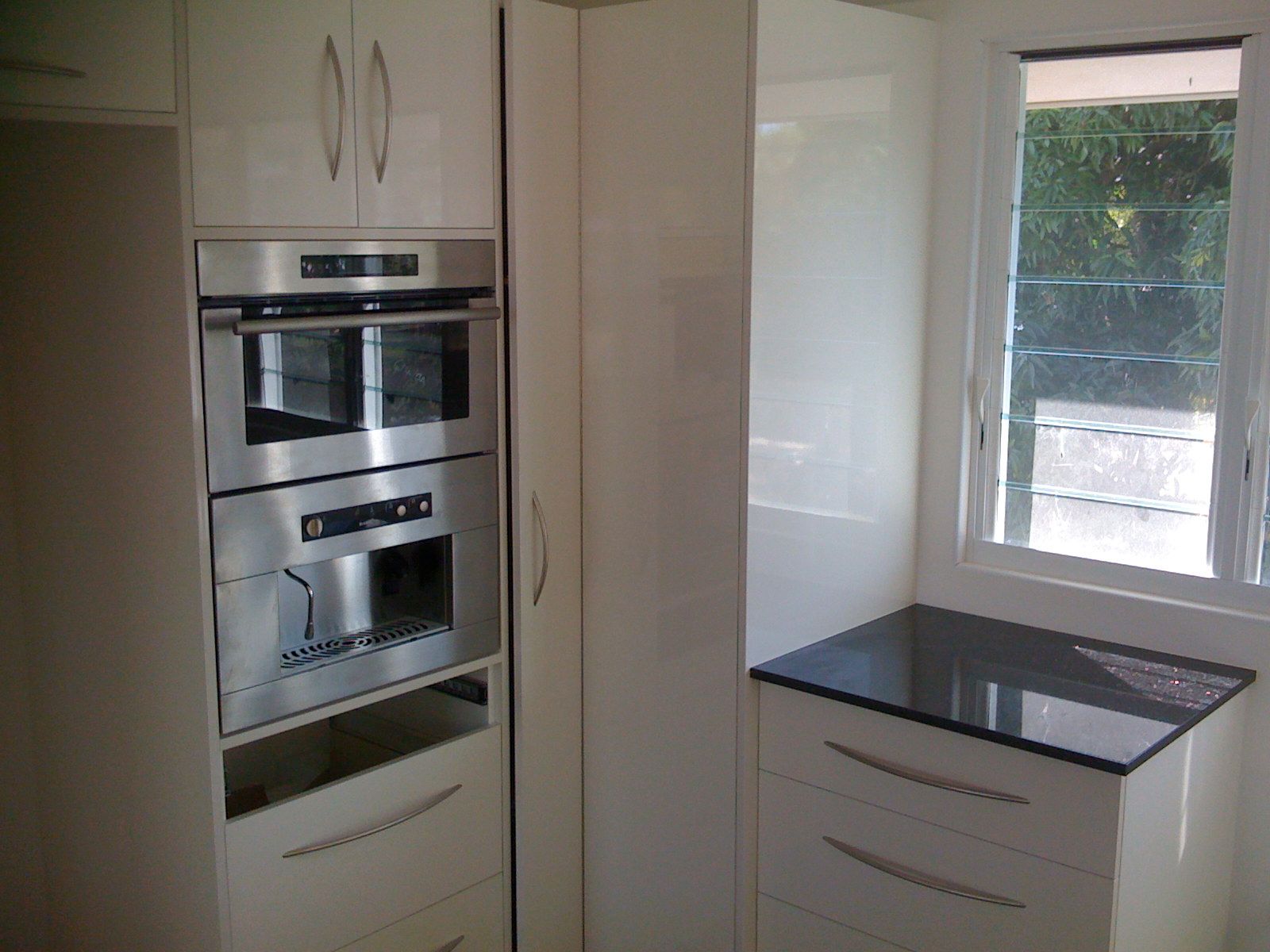 Modern White Kitchen with Built In Oven and Black Countertop by A Window — SS Building Services in Townsville, QLD