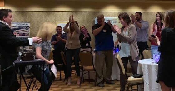 People clapping and dancing at an indoor party with chairs, tables, and a speaker setup