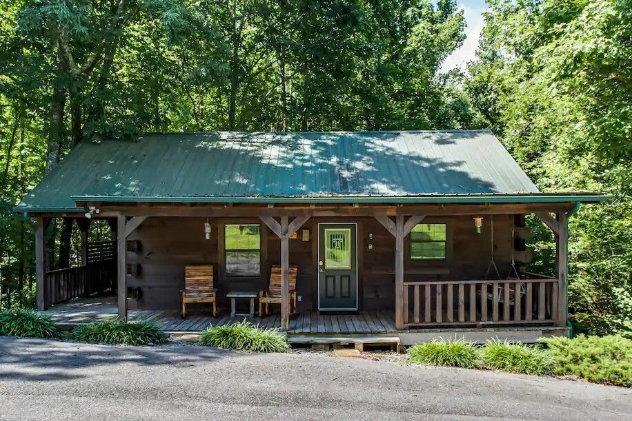 Small rustic cabin with green metal roof surrounded by trees and a porch