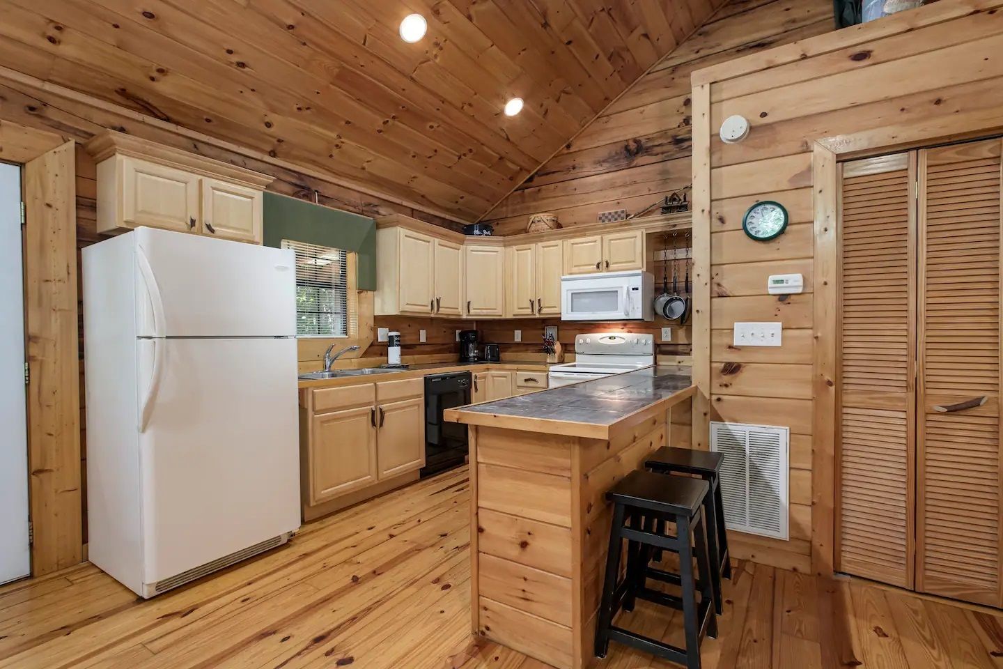 Cozy log cabin kitchen with white fridge, wood cabinets, island, and vaulted wood ceiling