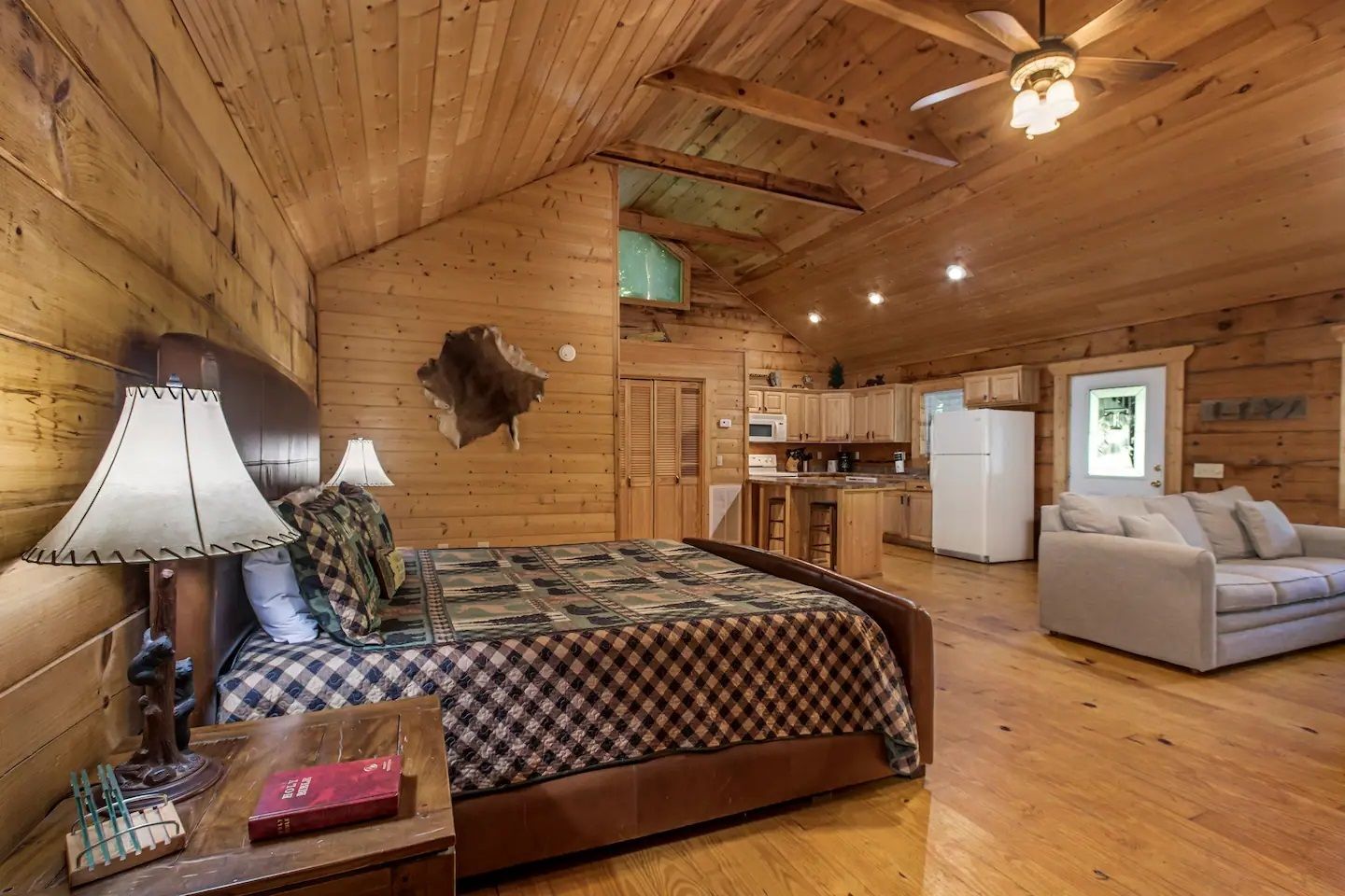 Cozy log cabin bedroom with a bed, sofa, lamp, and wood-paneled ceiling and walls