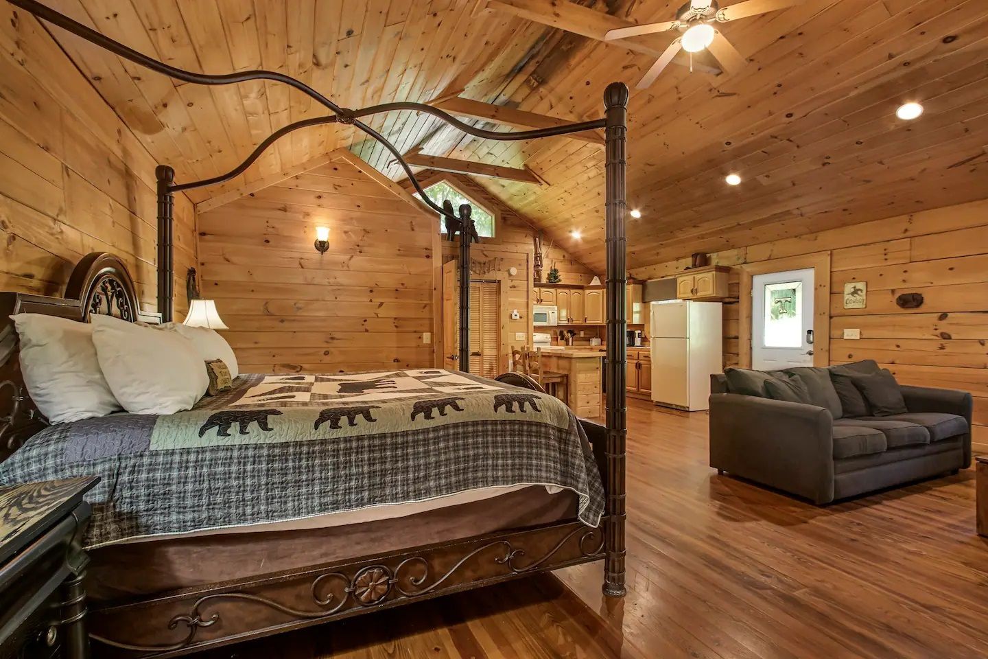 Rustic log cabin bedroom with wood walls, antler decor, bed, and a gray sofa near a doorway.