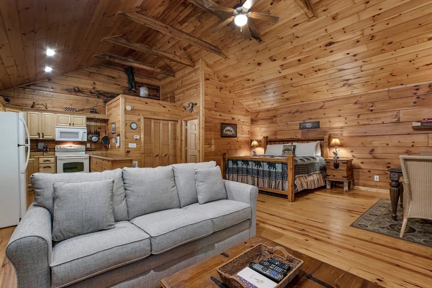 Cozy log cabin living room with gray sofa, wood-paneled walls, and open kitchen area