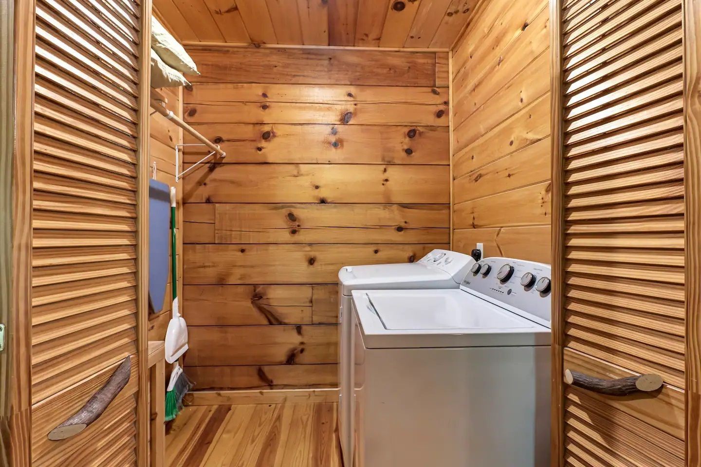 Wood-paneled laundry room with a white washer and dryer behind louvered doors