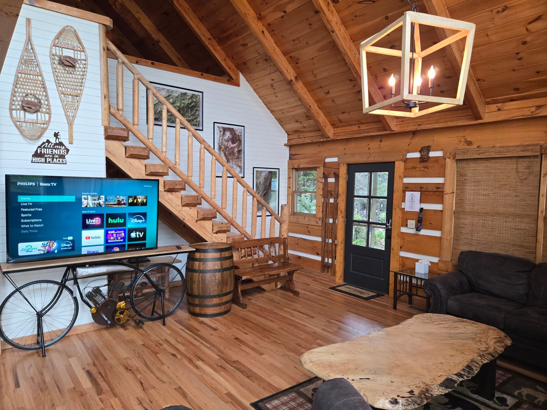 Cozy rustic cabin living room with TV, staircase, black couch, and wooden coffee table