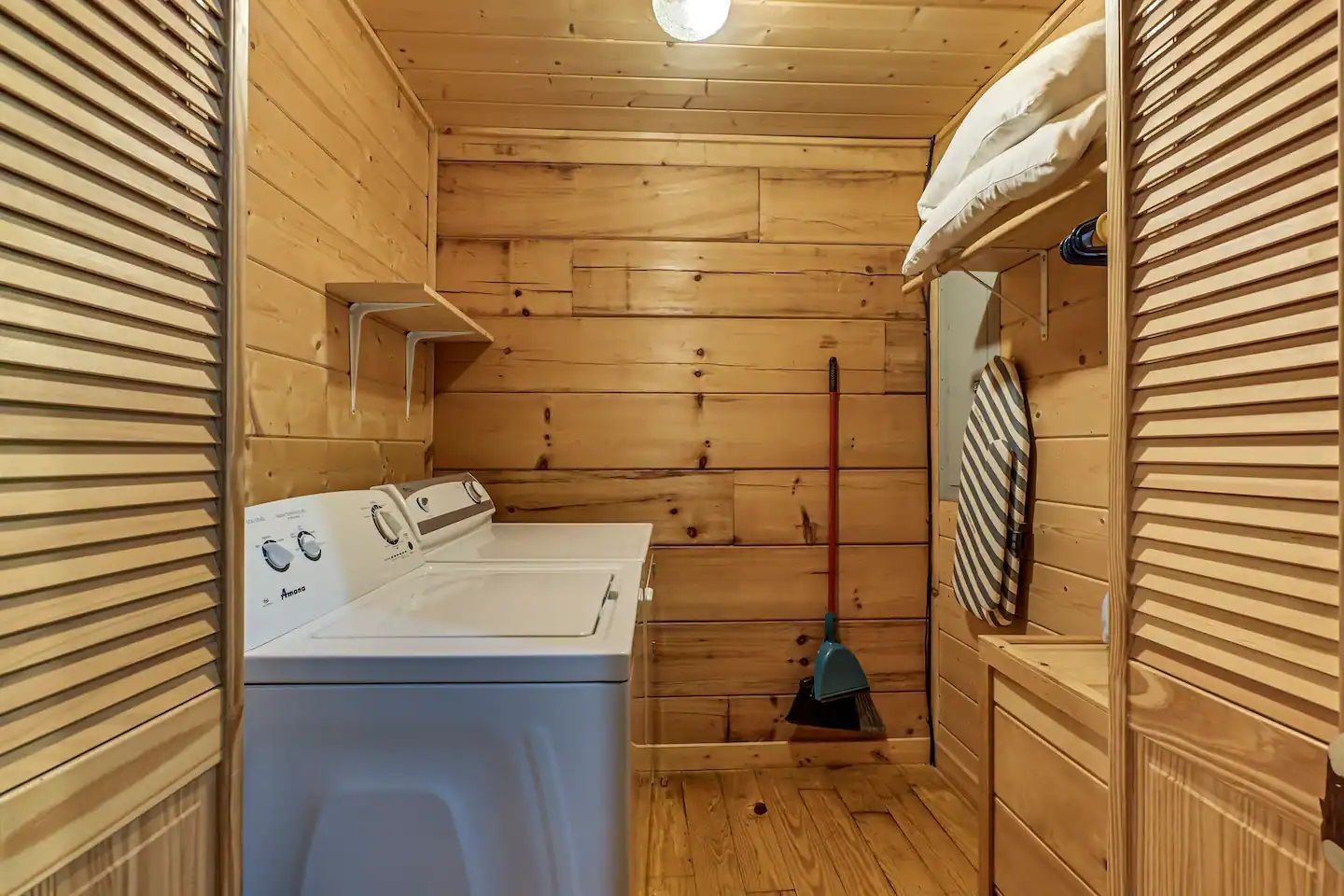 Laundry room with a washer, wooden walls, louvered closet doors, and folded towels on a shelf