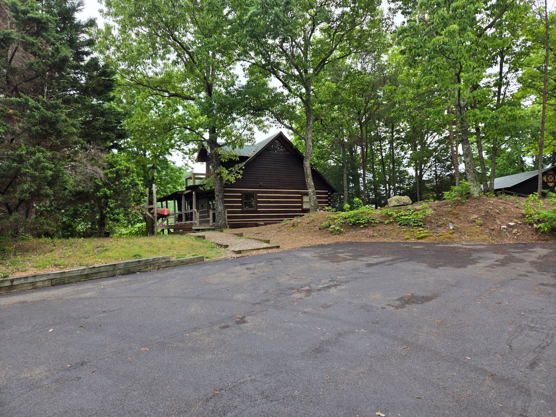 Small dark cabin in a wooded clearing beside a paved driveway