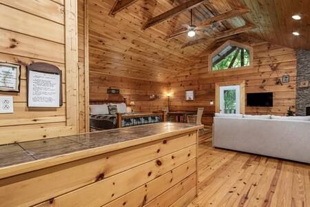 Wood-paneled cabin living room with kitchen counter, gray sofa, and vaulted ceiling above hardwood floors