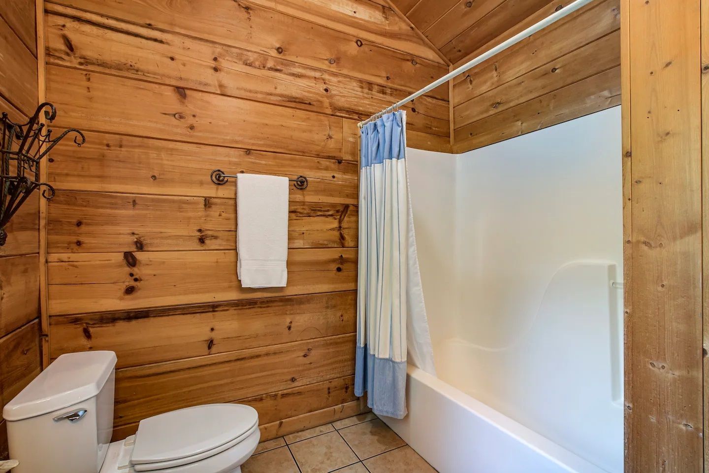 Rustic bathroom with wood-paneled walls, white tub, toilet, and blue shower curtain