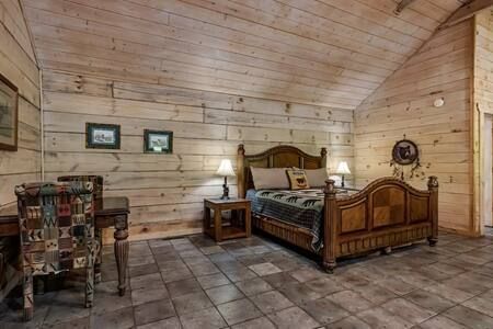Rustic log cabin bedroom with wood walls, tiled floor, two wooden beds, and a chair in the corner