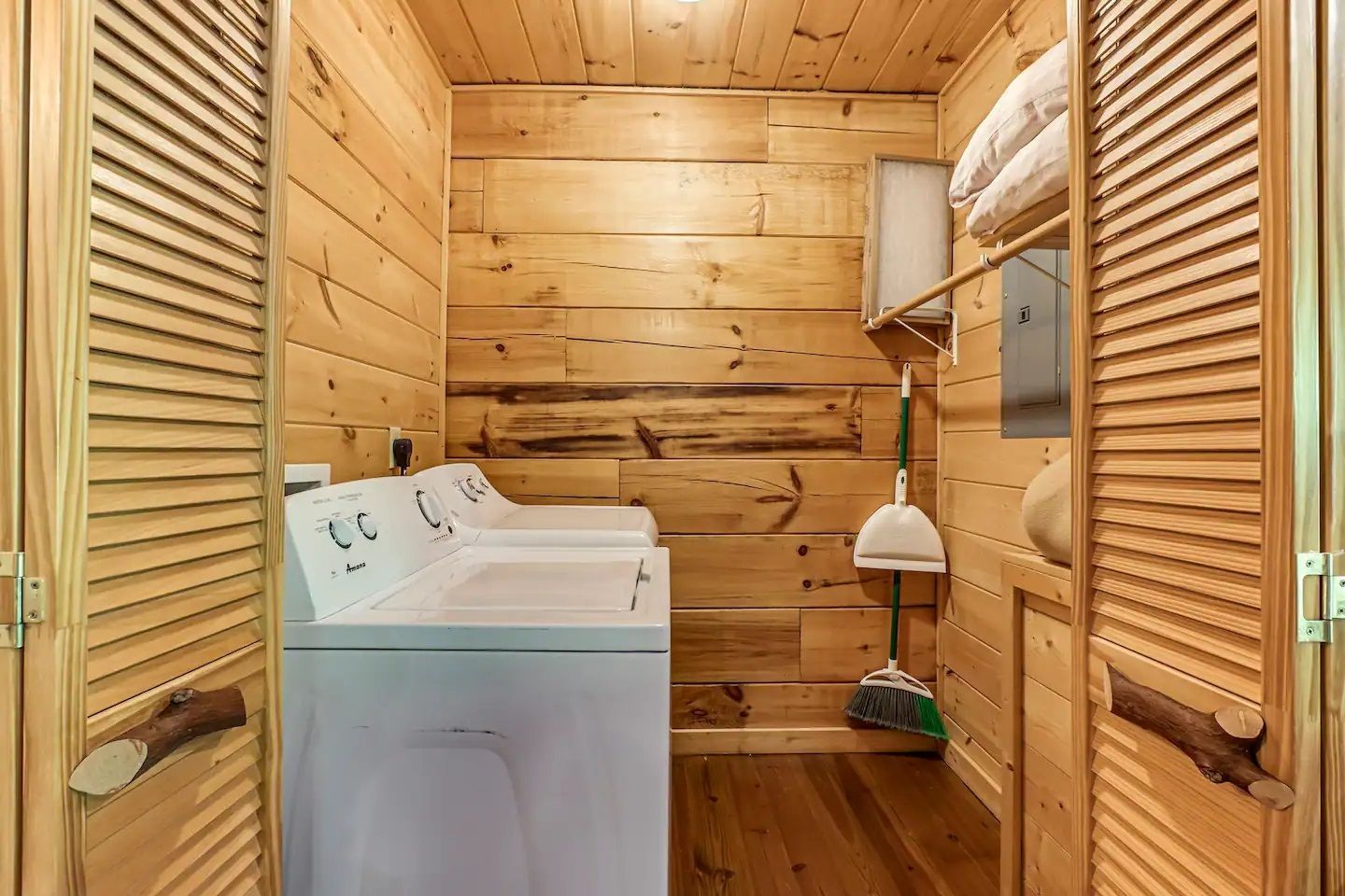 Small wooden laundry closet with a washer, shelves, and cleaning supplies inside a narrow room.