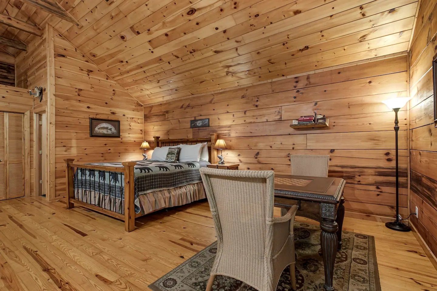 Wood-paneled rustic bedroom with a bed, desk, patterned rug, and floor lamp