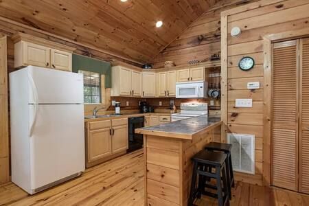 Wood-paneled kitchen with white appliances, light wood cabinets, and a small breakfast bar with stools