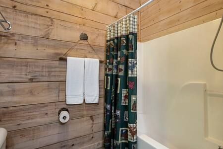 Wood-paneled bathroom with white towels, patterned shower curtain, and bathtub edge