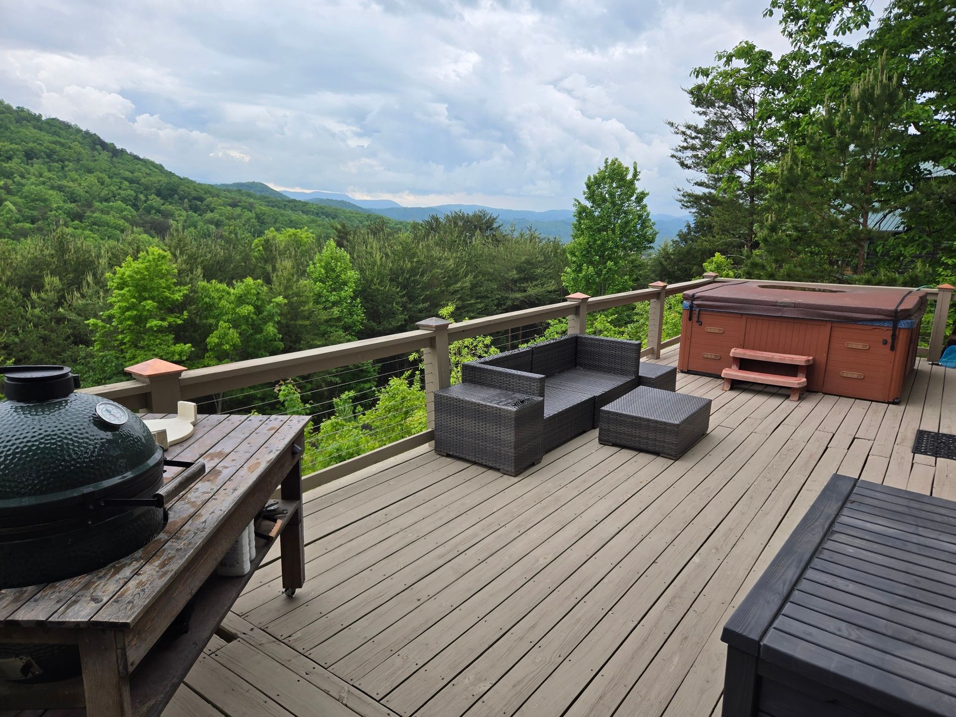 Wooden deck with black outdoor furniture and a hot tub overlooking a lush green mountain view