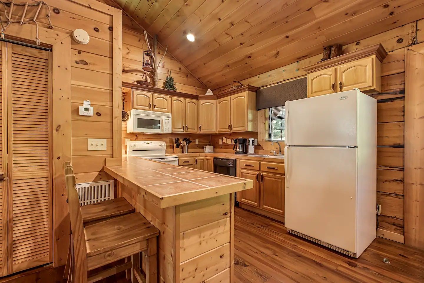 Cozy wood-paneled kitchen with pine cabinets, white fridge, and microwave under a sloped ceiling.