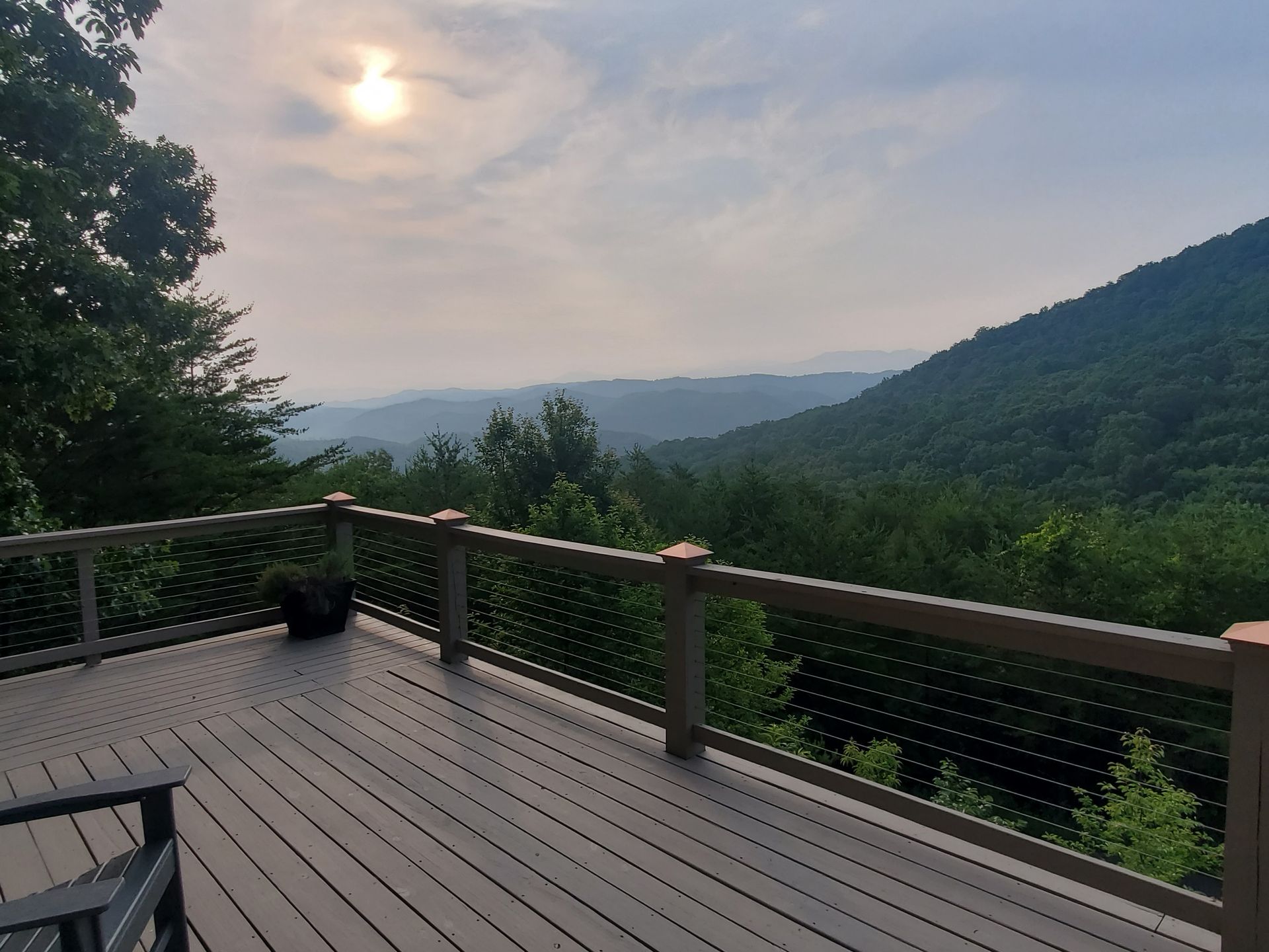 Deck overlooking a misty green valley at sunset, with mountains and a railing in the foreground