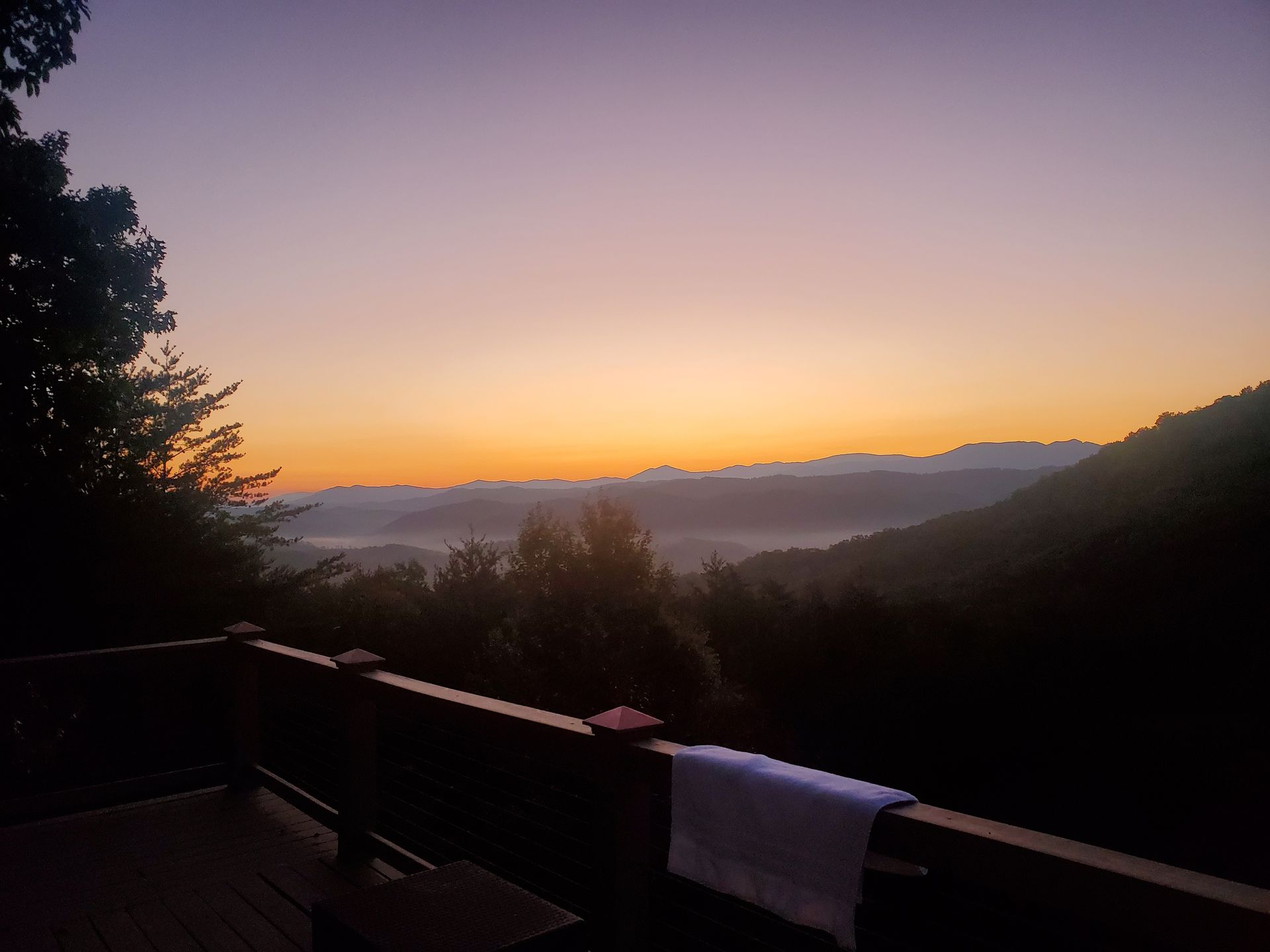 Sunset over misty mountains, seen from a deck with a railing and towel in the foreground