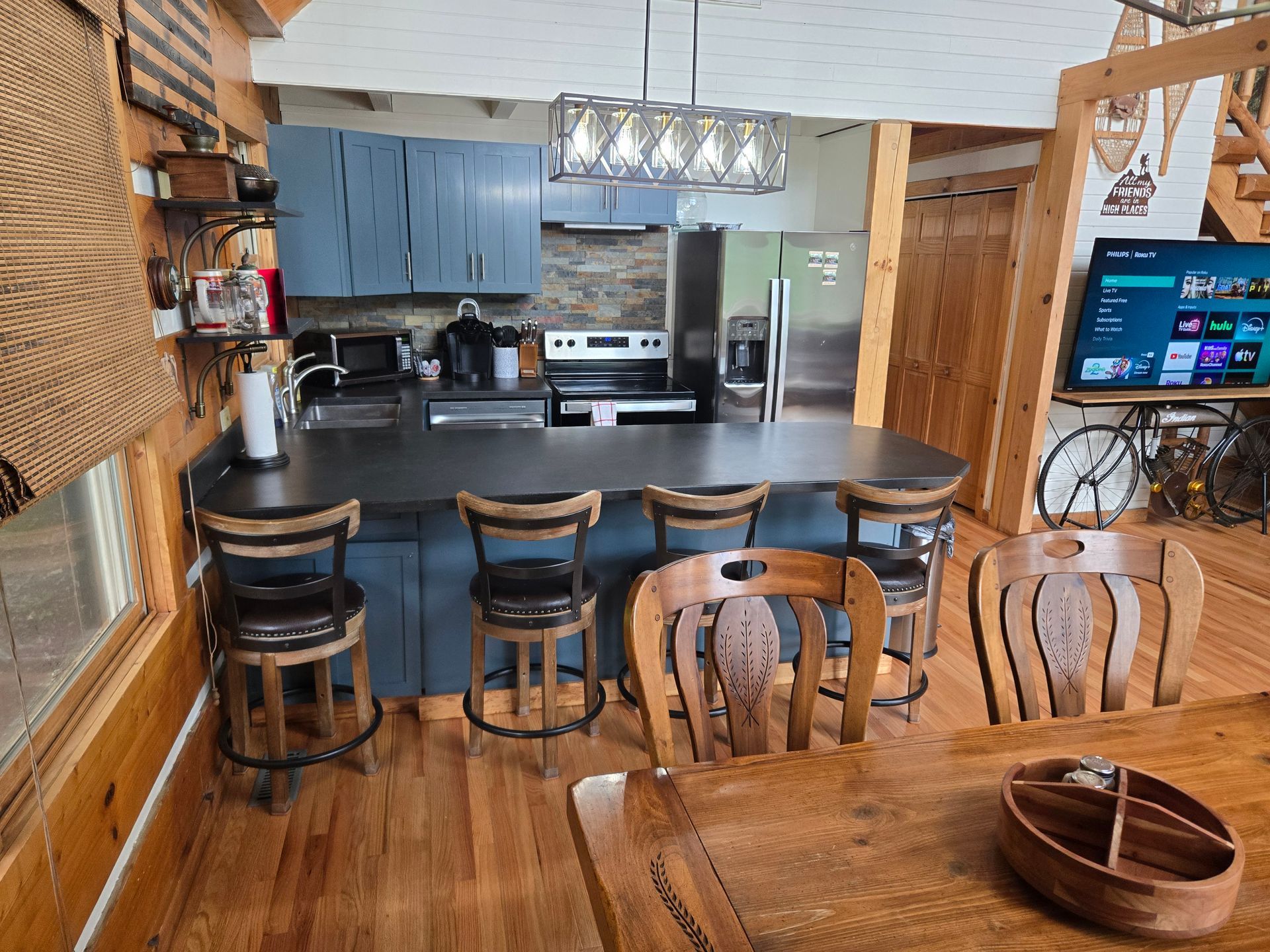 Cozy rustic kitchen with blue cabinets, black island, bar stools, and stainless steel appliances