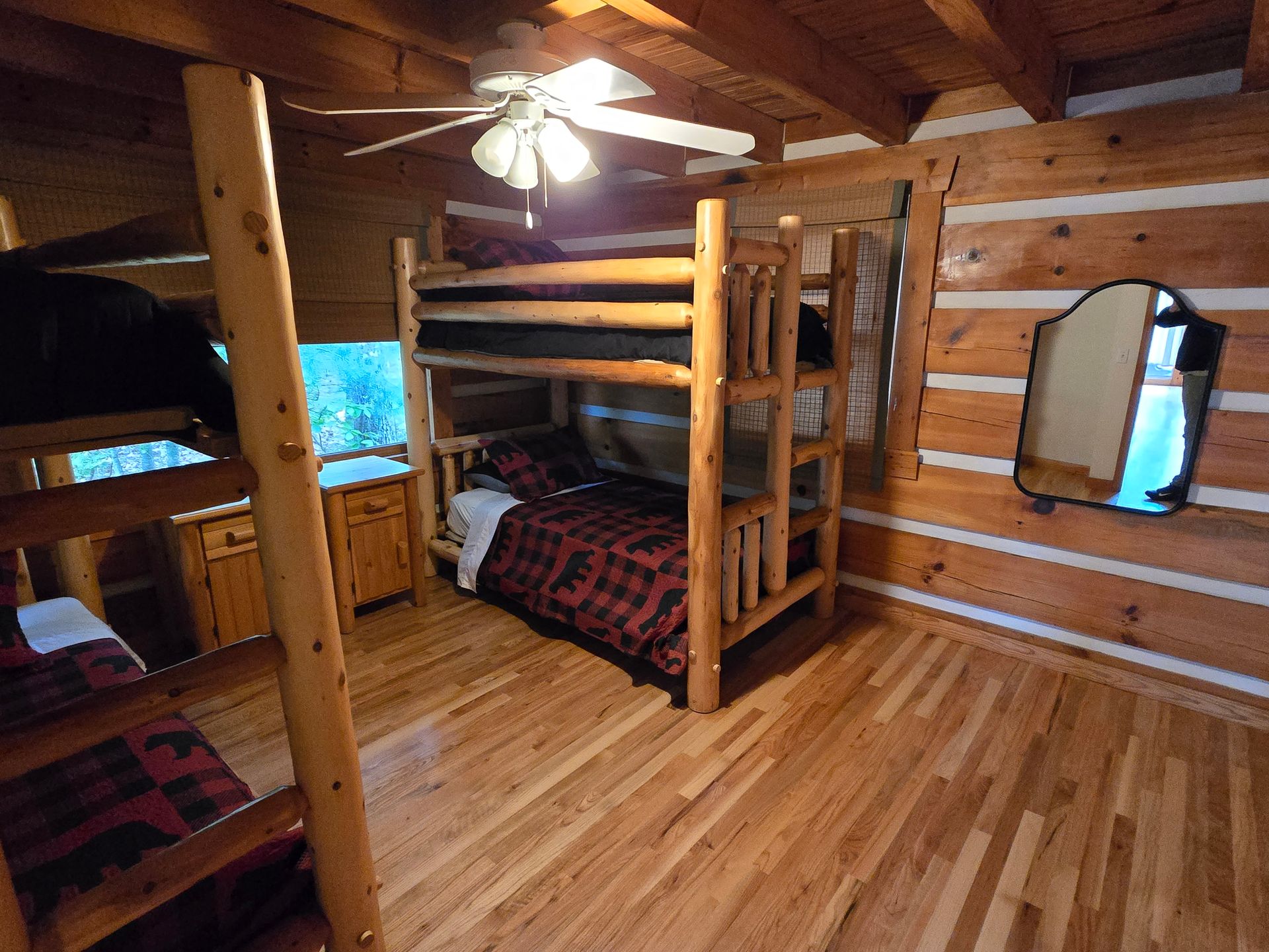 Rustic log cabin bedroom with wooden bunk beds, hardwood floors, and a ceiling fan.