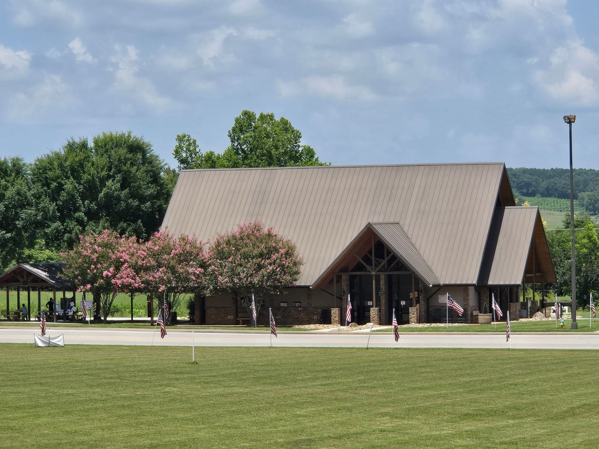 Large wooden lodge with steep roof beside blooming trees in a green park under a clear sky