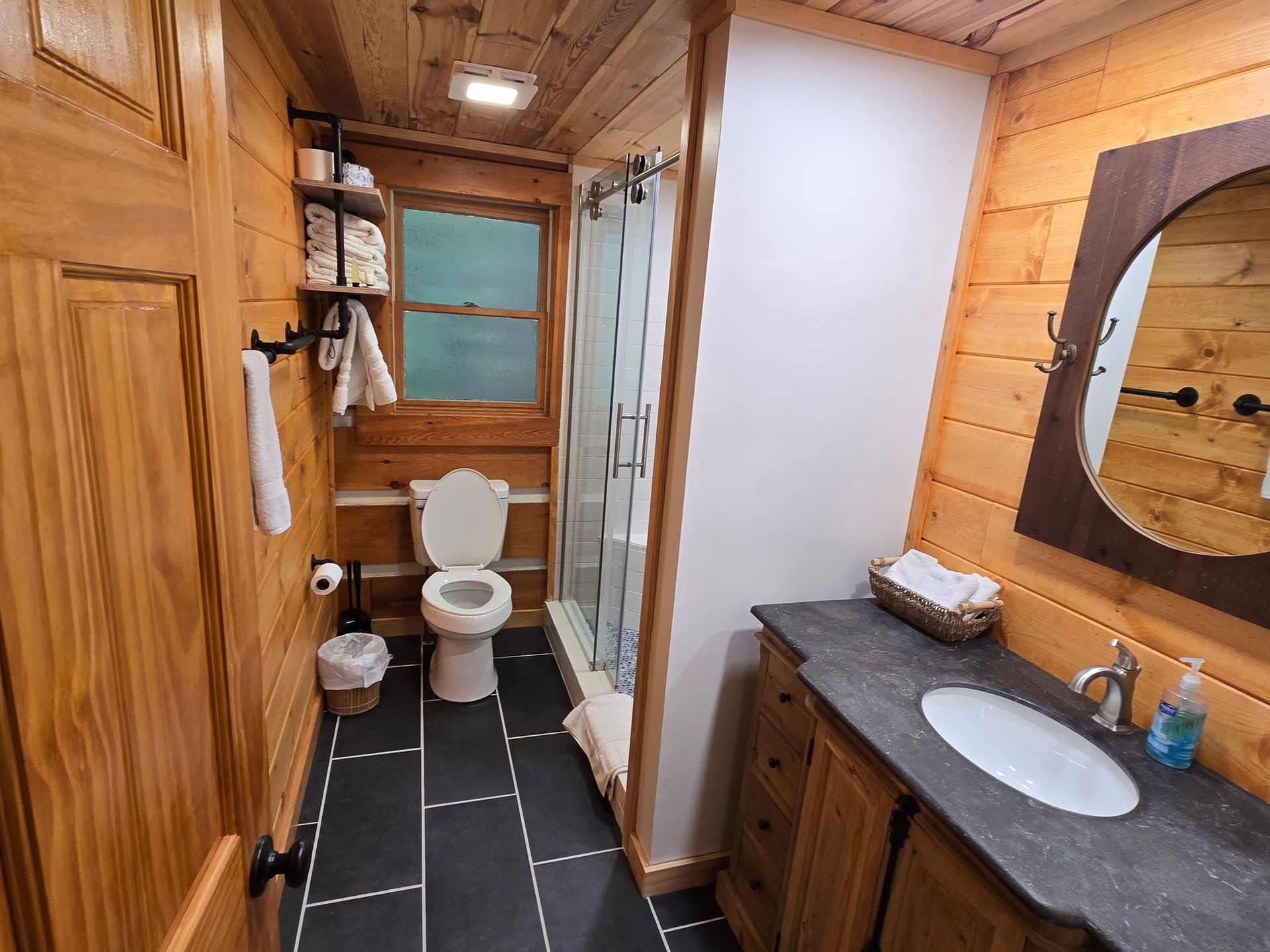 Rustic bathroom with toilet, sink, shower, and dark tile floor in a wood-paneled cabin