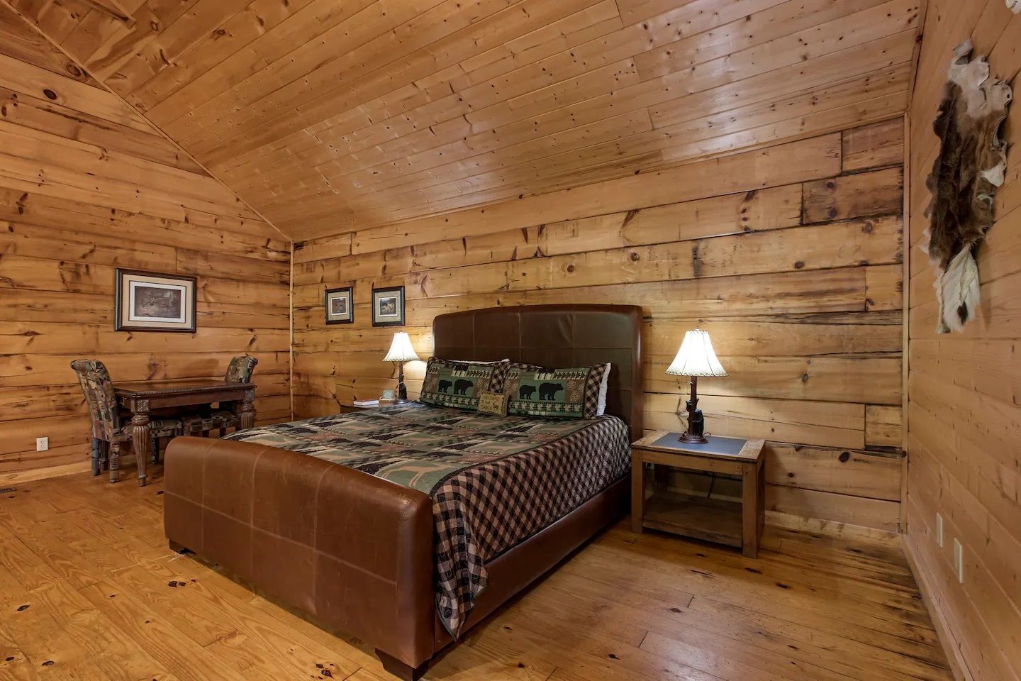 Wood-paneled rustic bedroom with a bed, nightstands, lamps, and framed wall art