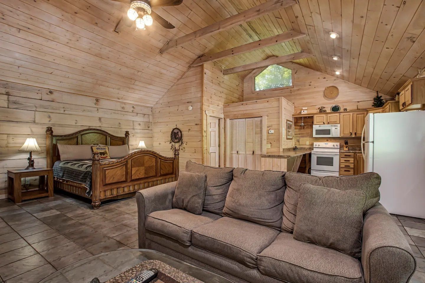 Rustic log cabin living room with wood ceiling, sofa, bed, fireplace, and kitchen area