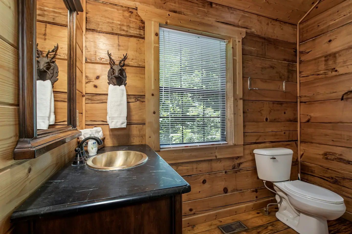 Rustic wood-paneled bathroom with sink, mirror, window, and toilet