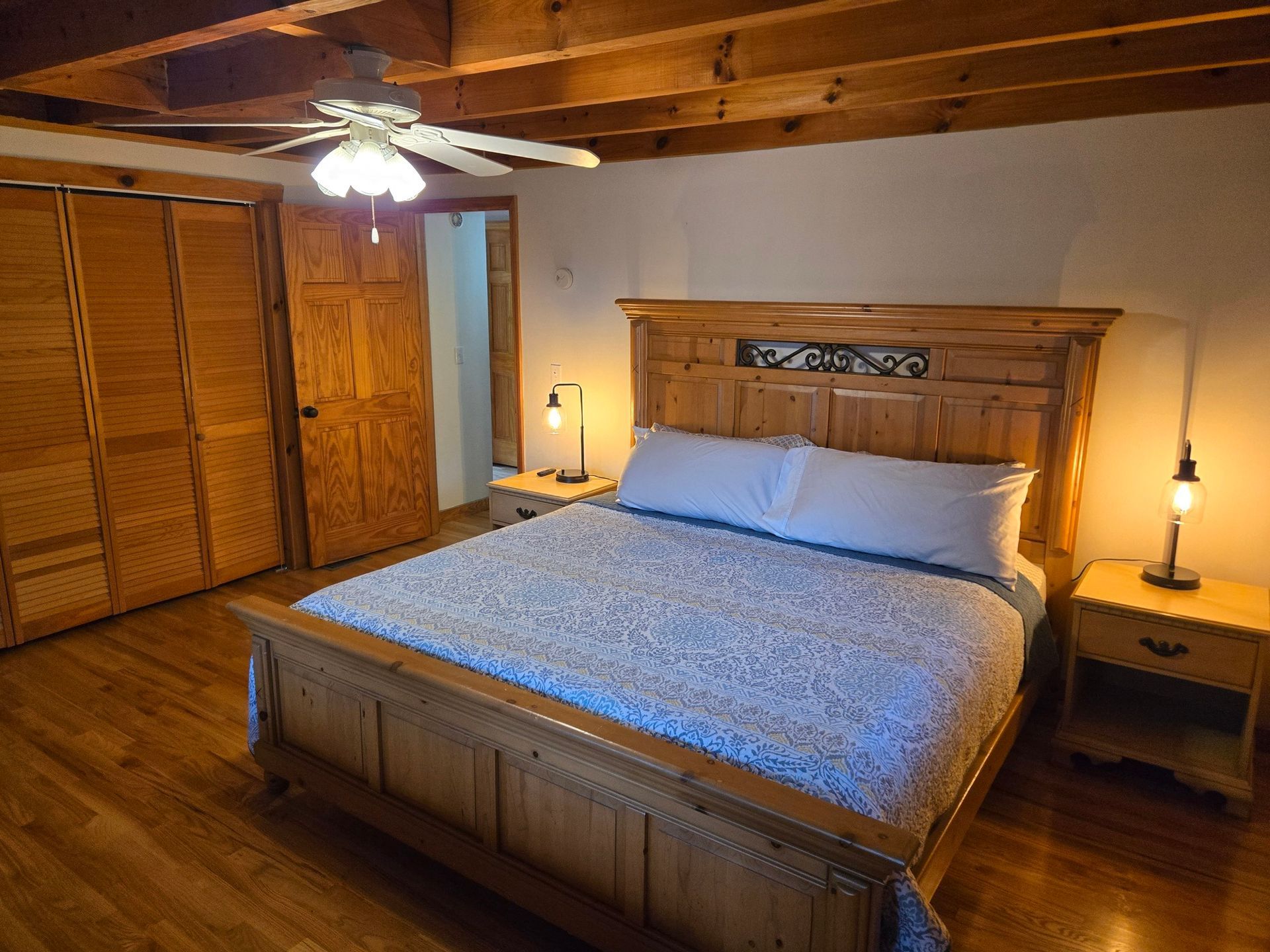 Cozy bedroom with wooden bed frame, blue bedding, nightstands, ceiling fan, and closet doors