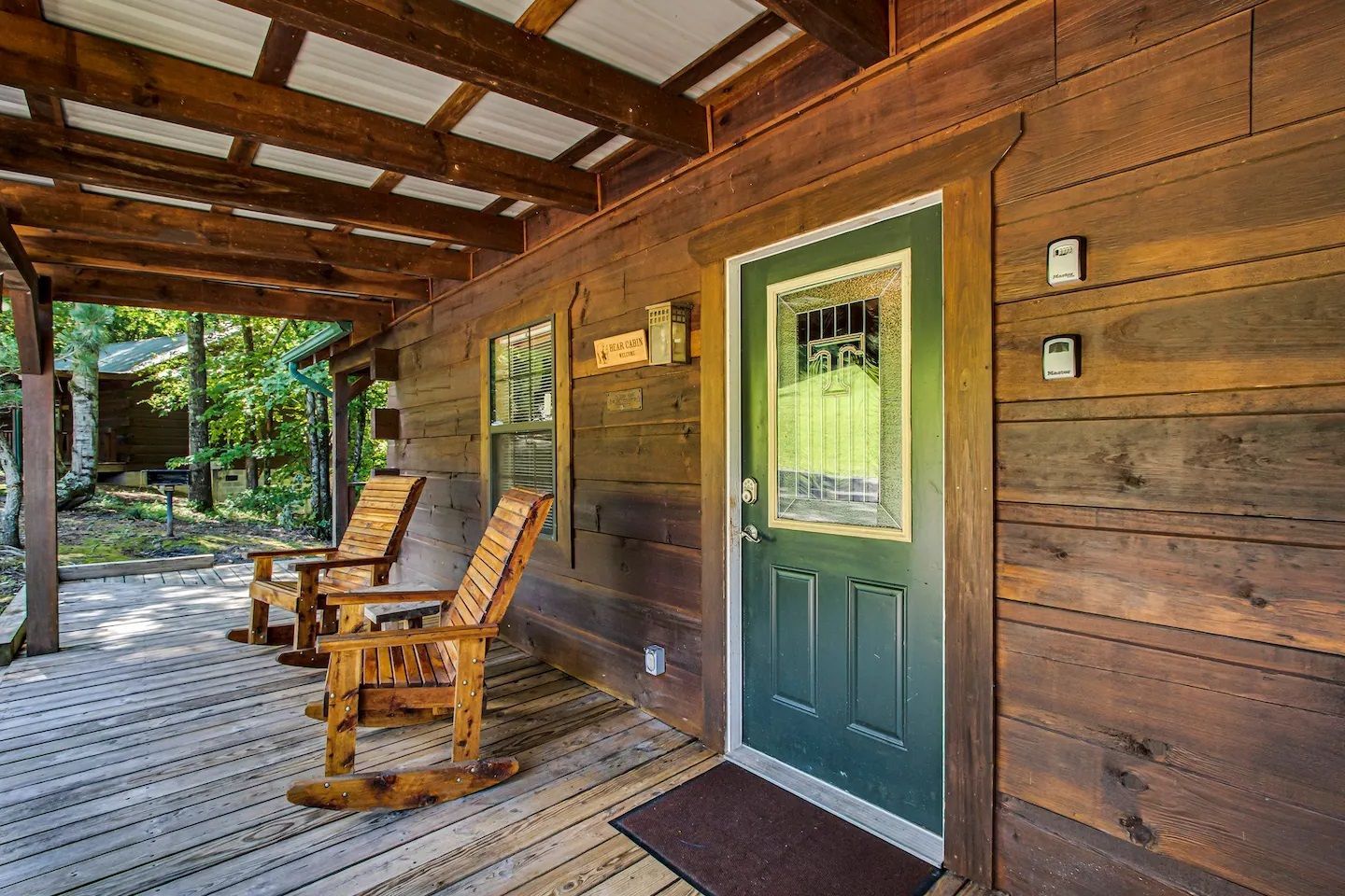 Covered wooden porch with green door, rocking chairs, and rustic cabin siding