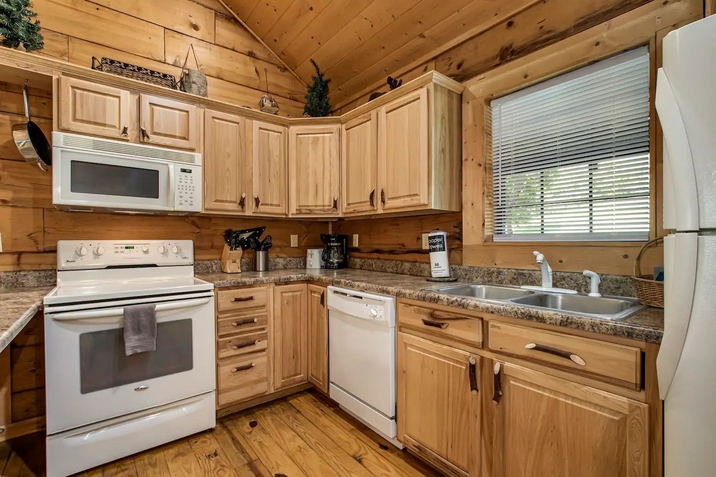 Wooden kitchen with white appliances, pine cabinets, and a large window above the sink