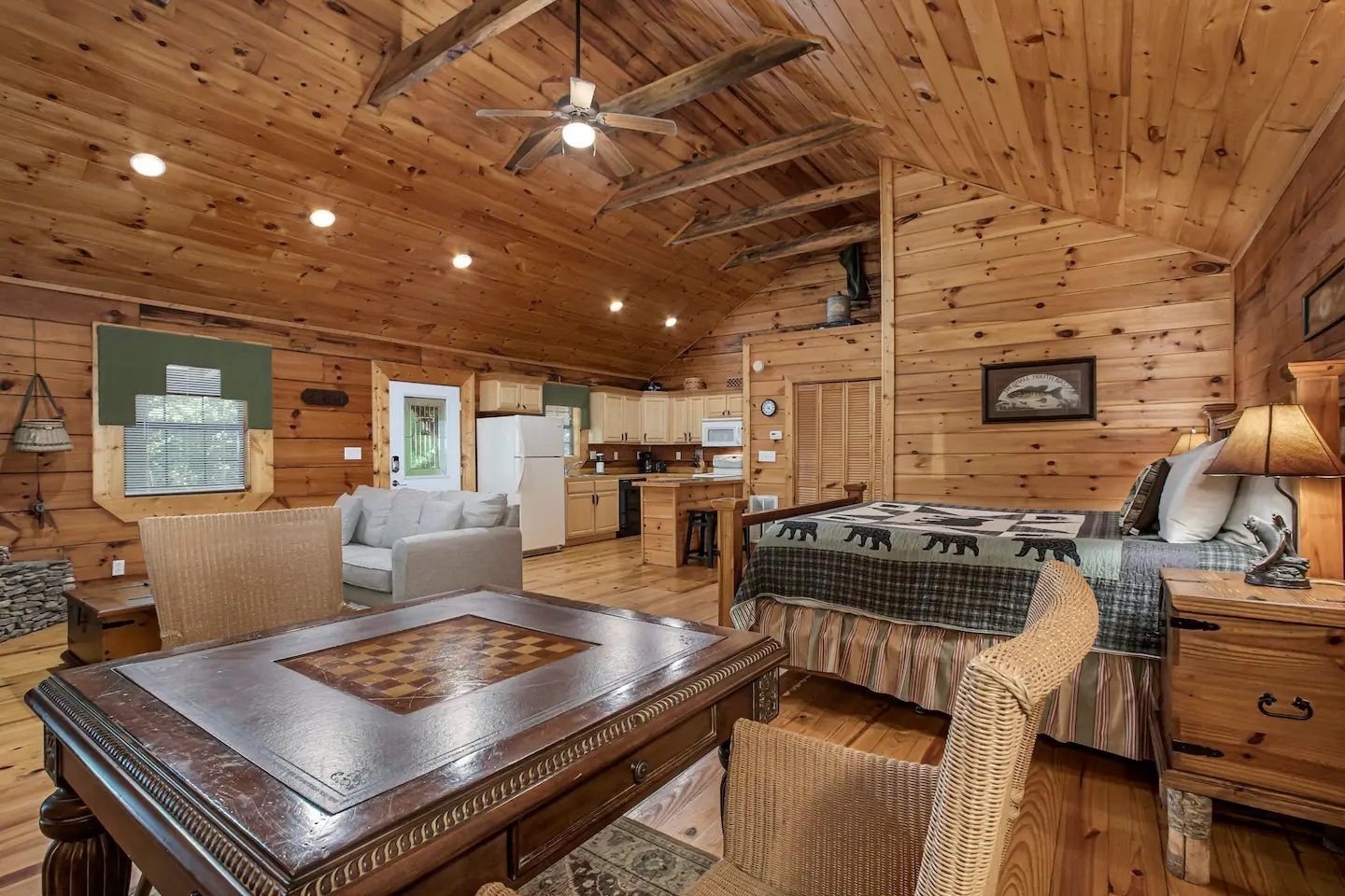 Cozy wood-paneled cabin living room with vaulted ceiling, leather chairs, lamp, and stone fireplace
